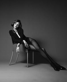 Woman in a black bodysuit and tights posing on a chair in black and white