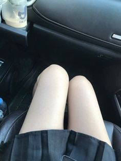 Person's legs in a car interior with a black skirt and drinks