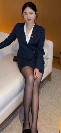 Woman in a dark suit jacket, mini skirt, and black pantyhose sitting indoors