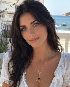 Woman with long dark hair and blue eyes wearing a white top and moon pendant necklace