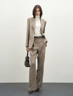 Woman in a pinstripe suit and white turtleneck holding a handbag