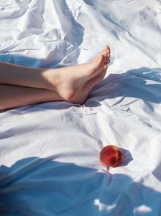 Bare legs and a peach on white sheets with strong sunlight and shadows