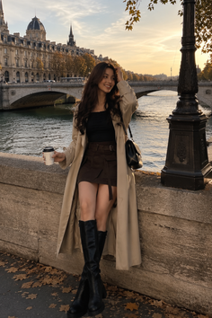 Woman in a trench coat and mini skirt by a river at golden hour