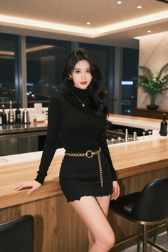 Woman in a black dress with a gold chain belt in an indoor setting at night