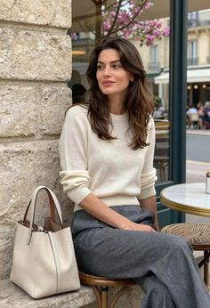 Woman with long hair in a white sweater and grey pants at an outdoor cafe
