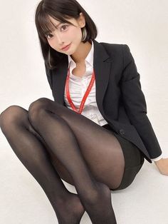 Woman in a black blazer and tights with a red lanyard, sitting on the floor