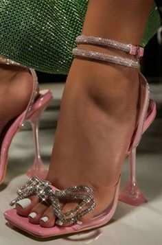 Close up of a foot wearing pink high heels with rhinestone bows and ankle straps