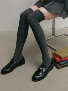 Person wearing thigh-high socks, a pleated skirt, and loafers, sitting indoors