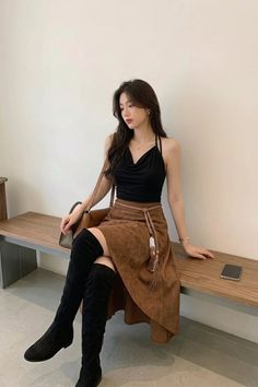 Woman with long hair wearing a black top and brown skirt with thigh-high boots