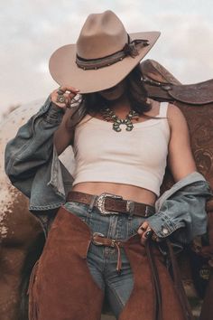 Woman in a cowboy hat, denim jacket, and chaps with a turquoise necklace