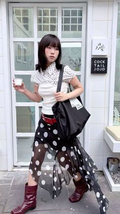 Woman in a polka dot shirt and skirt with red boots holding a cup outdoors