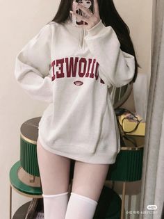 Person in an oversized sweatshirt and white socks, covering face with phone