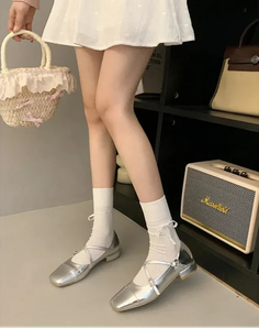 Person in a white dress and silver shoes holding a straw bag