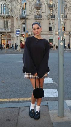 Woman in a black sweater and plaid skirt standing on a city street