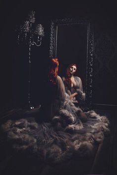 Woman with red hair in a sheer robe with feather trim looking in a mirror