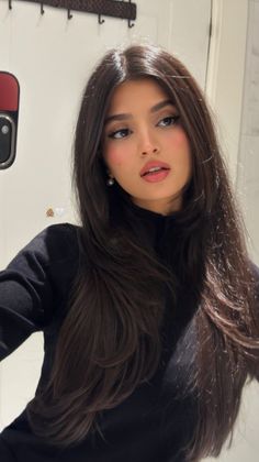 Woman with long dark hair wearing a black top and pearl earrings