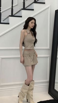 Woman with long dark hair wearing a crop top and mini skirt with knee-high boots indoors