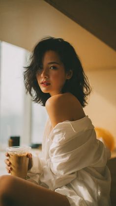 Woman with short hair in a white shirt holding iced coffee indoors