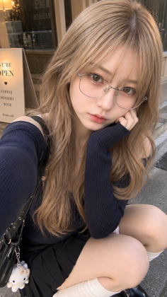Woman with long blonde hair and glasses in an off-shoulder top and pleated skirt
