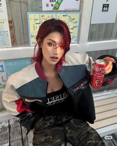 Woman with red hair in a bomber jacket and camo pants holding a soda can