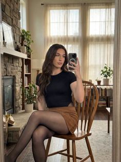 Woman with long brown hair taking a mirror selfie while sitting indoors