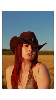 Woman in a cowboy hat and brown top with red hair outdoors at golden hour