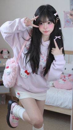Woman in a pink hoodie and white skirt with Hello Kitty accessories posing indoors