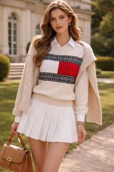 Woman in a sweater and white pleated skirt holding a brown handbag outdoors