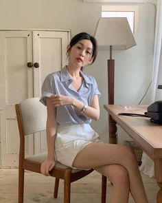 Woman in a striped shirt and white shorts sitting indoors