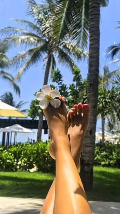 Crossed legs with red nail polish and a white flower against a tropical background