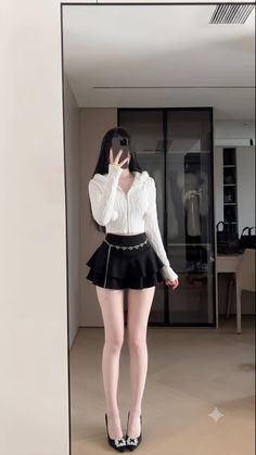 Woman in a white hoodie and black mini skirt taking a mirror selfie