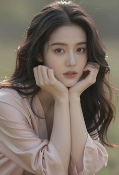Woman with long dark hair in a pink top, resting her chin on her hands outdoors