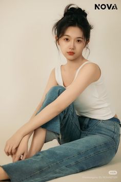 Young woman in a white tank top and blue jeans with a messy bun, sitting indoors