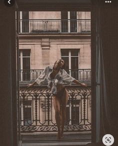 Woman in a white shirt and underwear on a balcony overlooking a cityscape