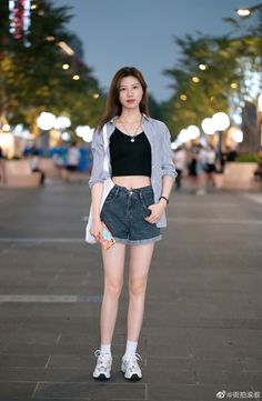Woman in a crop top, denim shorts, and striped shirt on a street at night