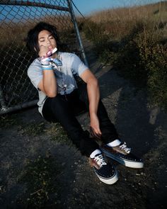 Person with long hair sitting on the ground next to a chain link fence