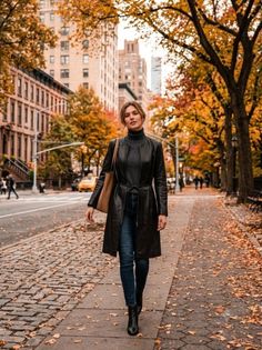 Woman in a black leather coat and jeans walking on a city street in autumn