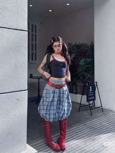 Woman in a plaid skirt, red boots, and crop top outdoors