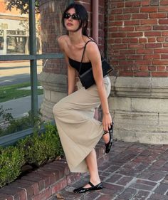 Woman in a black top and beige pants adjusting her shoe outdoors