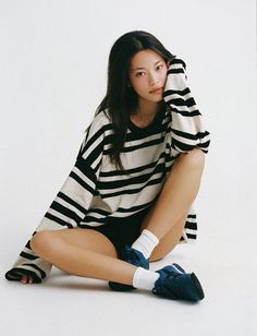 Woman with long dark hair wearing a striped shirt and shorts, sitting on a white background