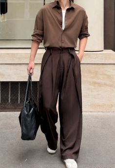 Person in a brown shirt and wide leg pants holding a black tote bag