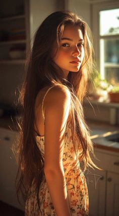 Woman with long hair in a floral dress bathed in golden hour light indoors