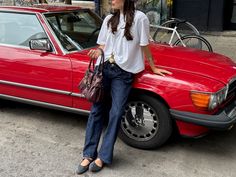 Woman in a white t-shirt and jeans leaning on a red car