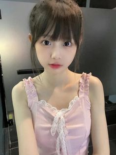 Young woman with dark hair and bangs wearing a pink top with lace trim