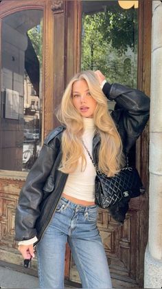 Blonde woman in a leather jacket and jeans posing outdoors
