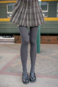 Person wearing a plaid skirt, thigh-high socks, and black loafers outdoors