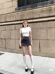 Woman in a crop top and mini skirt with knee-high socks standing outdoors
