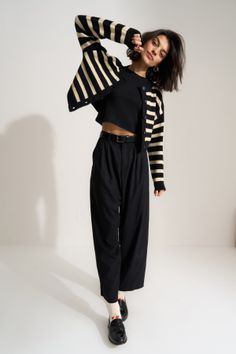 Woman in a striped cardigan, black crop top, and wide leg pants posing in a studio