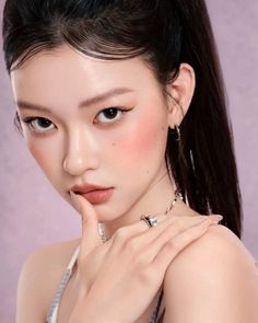 Woman with a ponytail and jewelry posing against a pink background