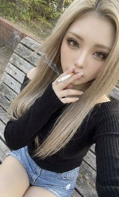 Woman with long blonde hair and denim shorts sitting outdoors and smoking